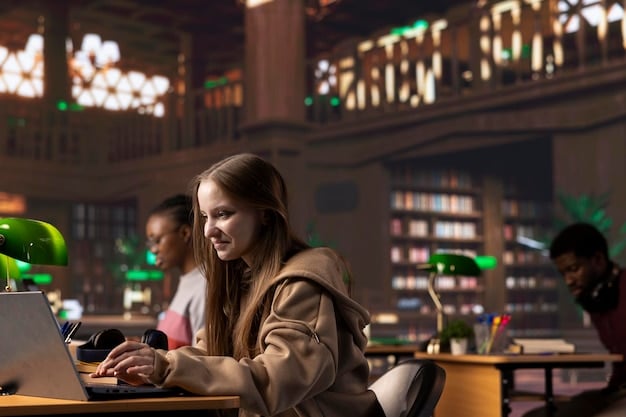A student is working on a laptop in a brightly lit library. They have a focused expression, with books and notebooks scattered around them. The background is filled with other students studying, creating a bustling academic atmosphere. The photo conveys the idea of hard work and dedication to educational goals.
