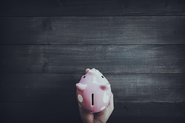 A piggy bank overflowing with dollar bills, with a hand adding more money to it. The background is blurred, focusing on the piggy bank representing savings and financial security.